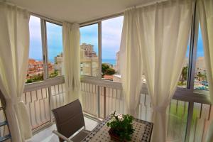 un balcón con cortinas blancas, una silla y una ventana en Apartamento Las Torres, en El Campello