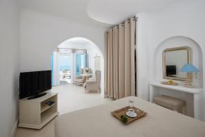 a white room with a bed and a tv and a chair at Andromeda Villas & Spa Resort in Imerovigli