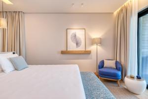 a bedroom with a white bed and a blue chair at Vathi Cove Luxury Resort & Spa in Chrysi Ammoudia