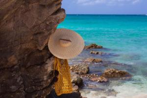 a straw hat hanging on a rock next to the ocean at Hôtel Barrière Le Carl Gustaf St Barth in Gustavia