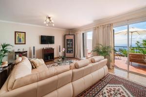 OurMadeira - Moradia da Falésia, panoramic views في كامارا دي لوبوس: غرفة معيشة مع أريكة كبيرة وإطلالة على المحيط
