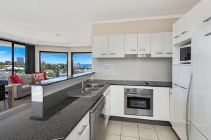 a kitchen with white cabinets and a living room at Mariners Resort Kings Beach in Caloundra