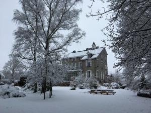 ein schneebedecktes Gebäude mit einem Picknicktisch und Bänken in der Unterkunft Beautiful manor house in a park near Rochefort in Forrières