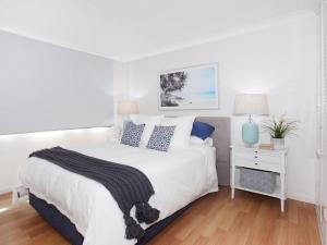 a white bedroom with a large bed and a nightstand at Windmill 4 Two Bedroom Beachside Apartment on Parkyn Parade in Mooloolaba