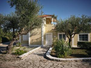 une maison jaune avec des arbres devant elle dans l'établissement Periyali Villas with Private Pools, à Vasilikos