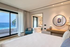 a bedroom with a large bed and a large window at Vathi Cove Luxury Resort & Spa in Chrysi Ammoudia