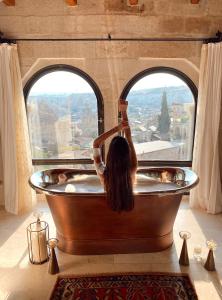 a woman in a bath tub looking out a window at Sultan Cave Suites in Göreme