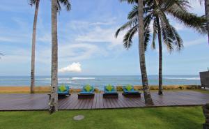una terraza con sillas, palmeras y el océano en Villa Samudra Luxury Beachfront, en Ketewel