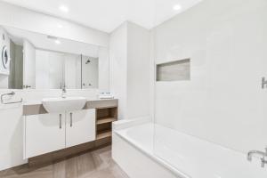 a white bathroom with a sink and a tub at Beachcomber on the Spit in Mooloolaba