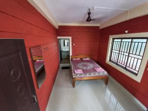 a room with a red wall with a bed and a window at Cocopelli Guest House in Gokarna