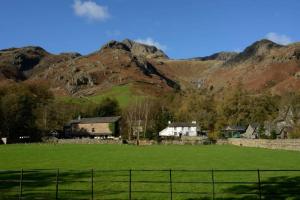 una granja con un campo y montañas al fondo en Stickle Cottage, Great Langdale, en Grasmere 9 fotos más