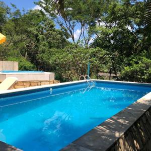 una piscina con agua azul y árboles en el fondo en Fazenda Quinta da Esperança- Pousada e Lazer, en Tiradentes