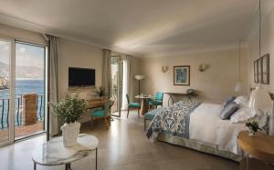 a living room with a bed, chair, table and window at Villa Sant'Andrea, A Belmond Hotel, Taormina Mare in Taormina
