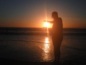 una mujer de pie en la playa mirando la puesta de sol en Apartamento Jamesson Cabo Frio en Cabo Frío