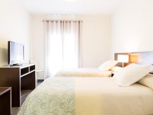 a white bedroom with two beds and a television at Hotel Madrid de Sevilla in Seville