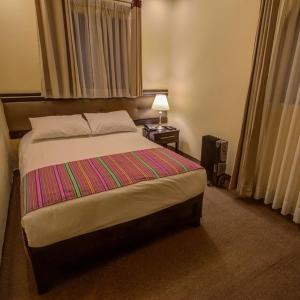 een slaapkamer met een bed en een nachtkastje met een lamp bij Tampu Hotel in Cuzco