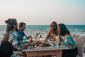 a group of people sitting at a table on the beach at The Cove Rotana Resort - Ras Al Khaimah in Ras al Khaimah