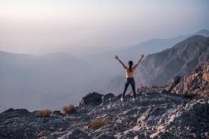 a woman standing on top of a mountain with her arms up at The Cove Rotana Resort - Ras Al Khaimah in Ras al Khaimah