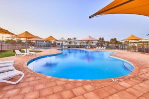 a patio area with a pool, chairs, and umbrellas at RAC Exmouth Cape Holiday Park in Exmouth