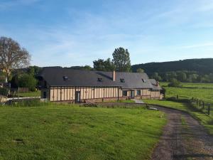 a large wooden barn in a field with a road at La Longère Des Nuits De Varenne in Muchedent