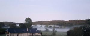 a barn in a field with fog in the background at La Longère Des Nuits De Varenne in Muchedent