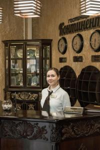 a woman standing behind a counter with clocks on the wall at Hotel Continent in Tobolsk