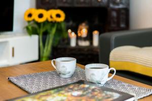 two cups on a table with a book and flowers at Exclusive Royal Apartments in Kraków