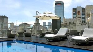 una piscina en la azotea con sillas y una sombrilla en un edificio en 725 Continental Hotel en Buenos Aires