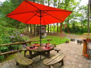 a picnic table with a red umbrella and two chairs at Chalet and gypsy caravan in a green and peaceful environment near Houffalize in Houffalize