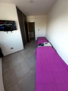 a room with two beds with pink sheets and a tv at Departamento nuevo 2 dorm, parrilla, cochera in Neuquén