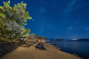 a row of benches and umbrellas on a beach at night at LaLiBay Resort & Spa - Adults Only in Perdika