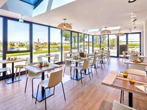 a restaurant with tables and chairs and windows at ibis La Roche Sur Yon Vendespace in Mouilleron-le-Captif