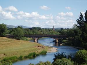 uma ponte sobre um rio ao lado de um campo em Warwick Hall em Carlisle