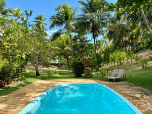 a blue swimming pool in a yard with palm trees at Pousada Capitù in Imbassai