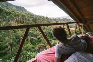 a woman sitting on a bed looking out at the forest at Creo Ecolodge Jardín in Jardin