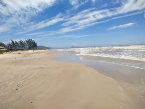 a sandy beach with waves and trees in the ocean at Casa Unamar Cabo Frio/RJ. in Cabo Frio
