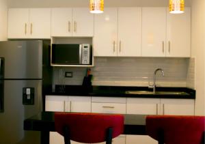 a kitchen with white cabinets and a microwave and red chairs at Suites Terraza Imperial in Guatemala