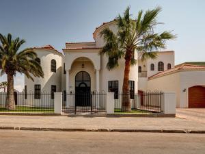 a white house with palm trees and a fence at Lagoon Suites Guesthouse CC in Walvis Bay