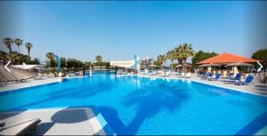 ein großer blauer Swimmingpool mit Liegestühlen und Palmen in der Unterkunft Doreta Beach in Theologos