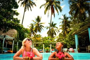 two women in bathing suits sitting next to a swimming pool at Butiama Beach Lodge in Kilindoni