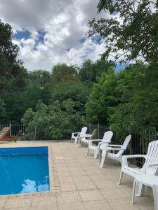 eine Reihe weißer Stühle neben einem Pool in der Unterkunft Cabañas Bosques del Centro in Mina Clavero