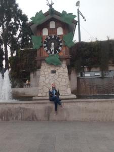 un homme assis sur un mur devant une tour d'horloge dans l'établissement Luminoso y bello departamento en Carlos Paz, à Villa Carlos Paz