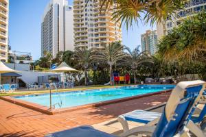 a swimming pool with chairs and palm trees and buildings at Chateau Beachside Resort in Gold Coast