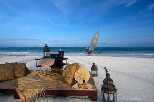 a bed on the beach with a boat in the ocean at The Palms Zanzibar in Bwejuu