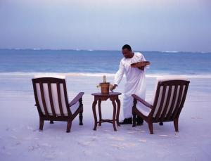 a man standing on the beach with a table and two chairs at The Palms Zanzibar in Bwejuu