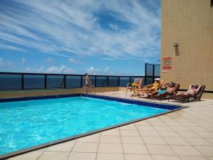 a pool on the roof of a building with people sitting in chairs at Farol da Barra 209 in Salvador