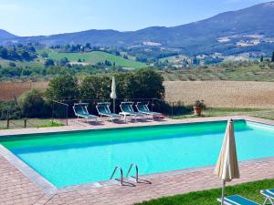 a swimming pool with chairs and umbrellas and a mountain at Villa Palazzo Bello con piscina e AC - Cetona in Cetona