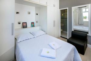 ein Schlafzimmer mit einem weißen Bett und einem schwarzen Stuhl in der Unterkunft Studio frente mar no Leme para 2 pessoas in Rio de Janeiro