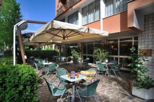un patio con mesas, sillas y una sombrilla en Hotel Atis, en Bellaria-Igea Marina