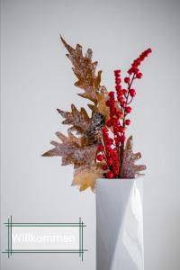 a white vase with leaves and red flowers in it at Kohlwies 